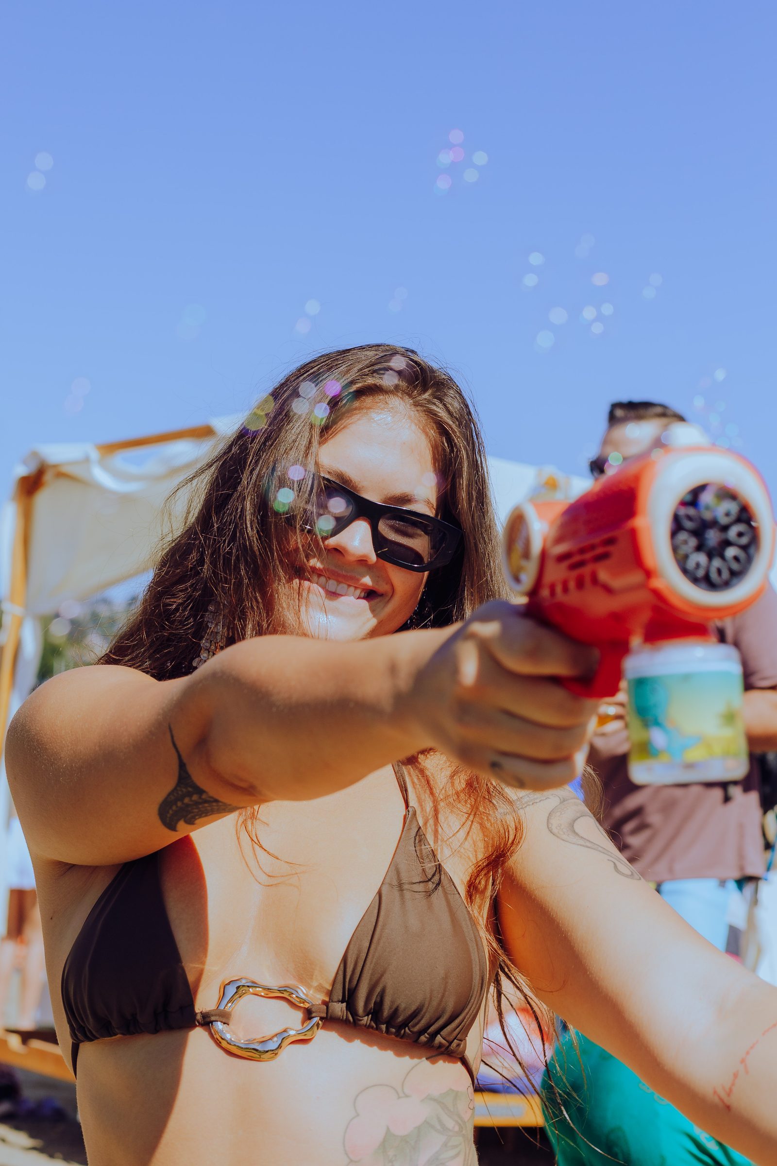 Woman in sunglasses laughing behind a bubble gun