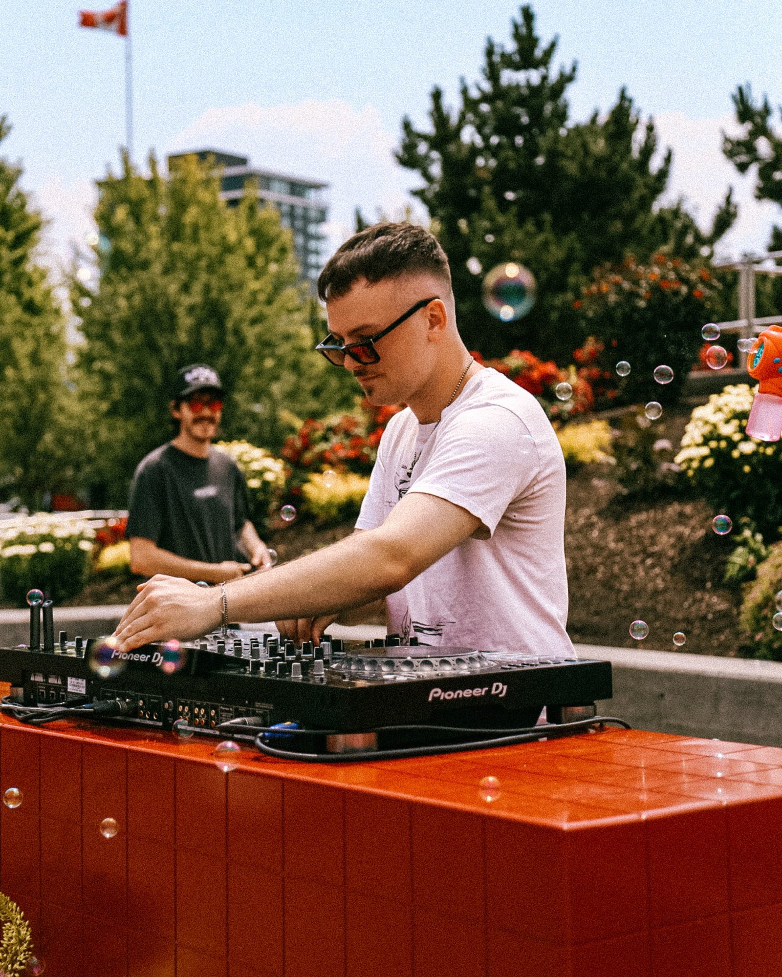 A DJ playing to a sunny crowd from a red booth