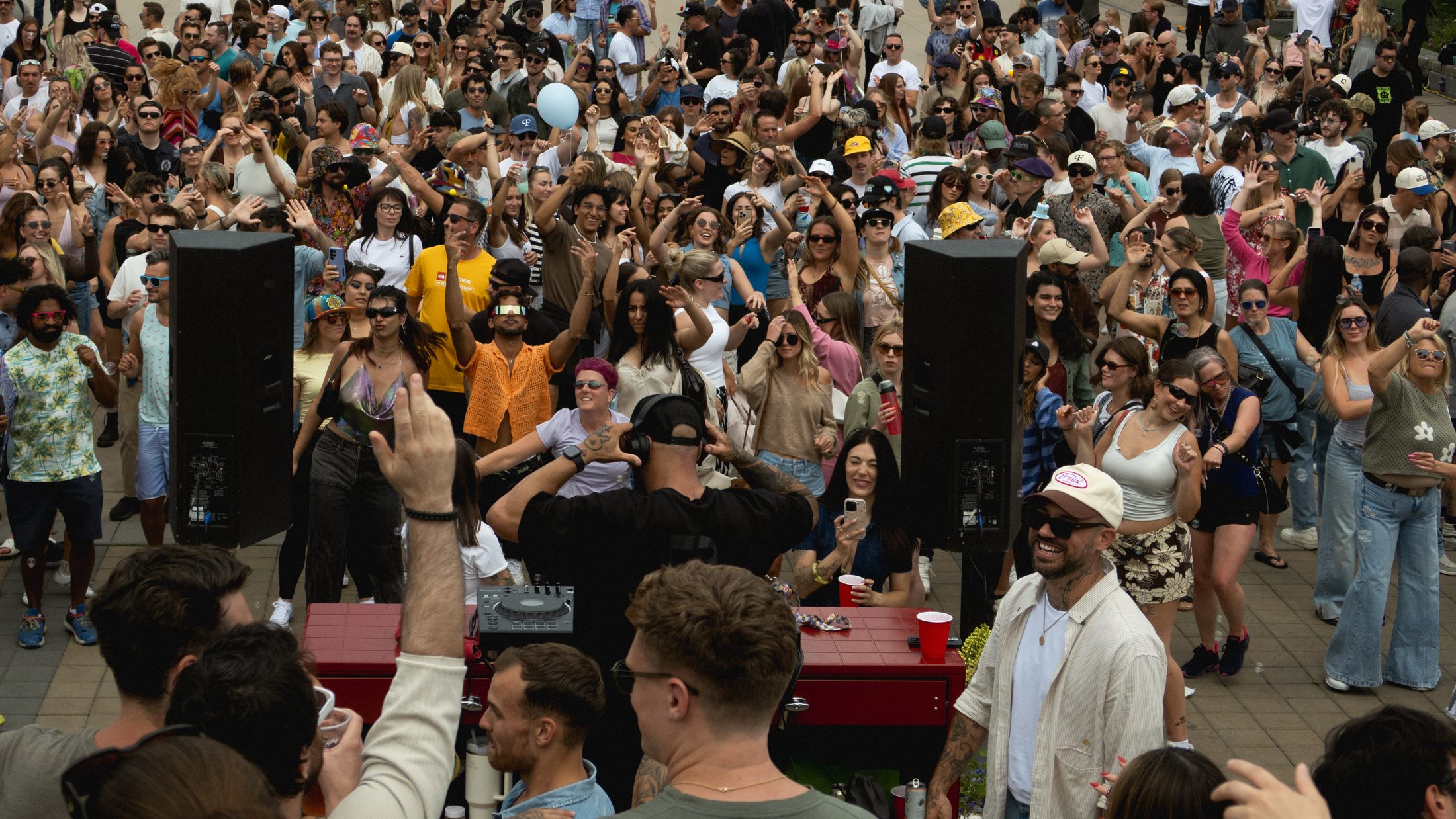 A packed daytime dancefloor with hands in the air under an open sky