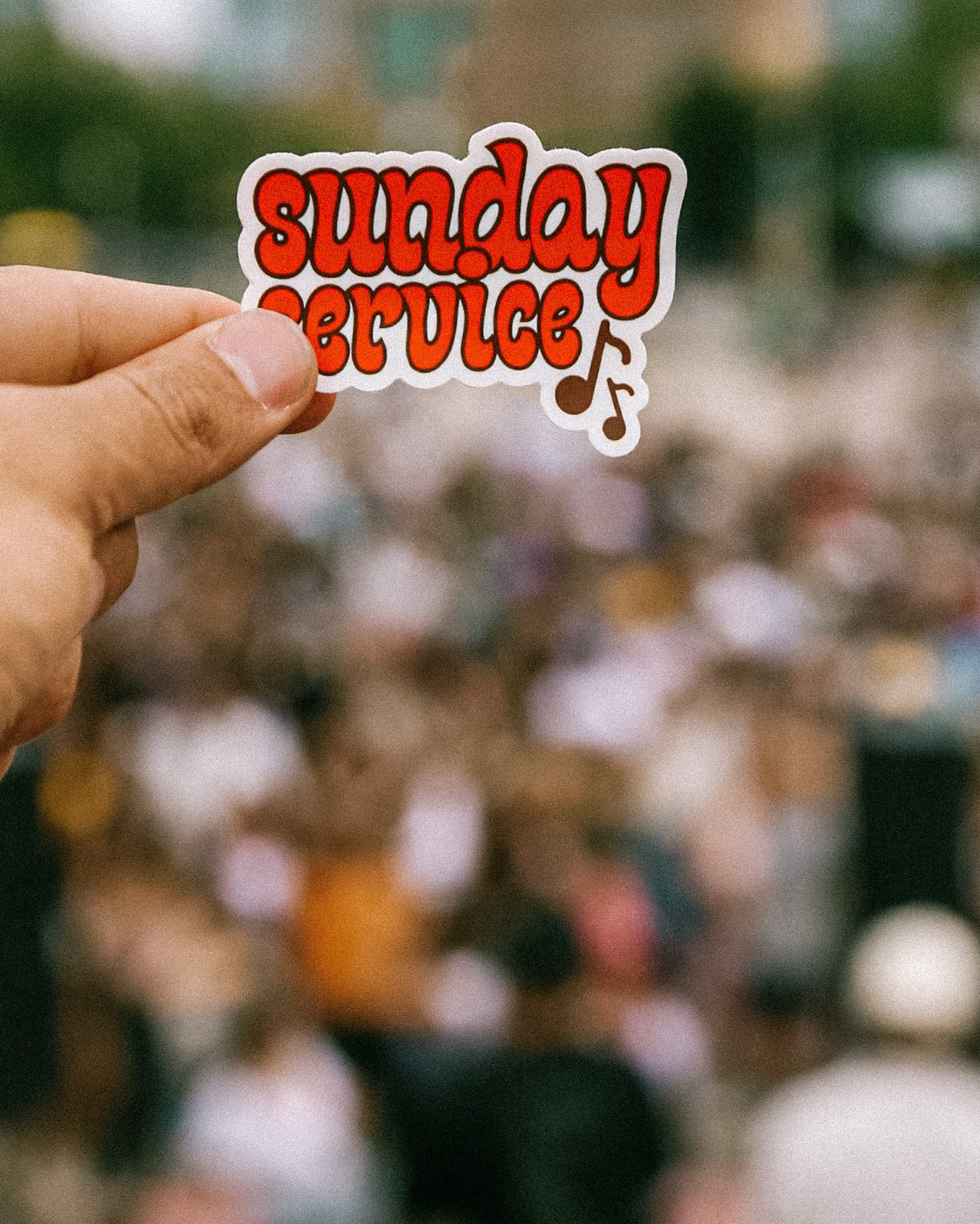 A hand holding a retro Sunday Service sticker