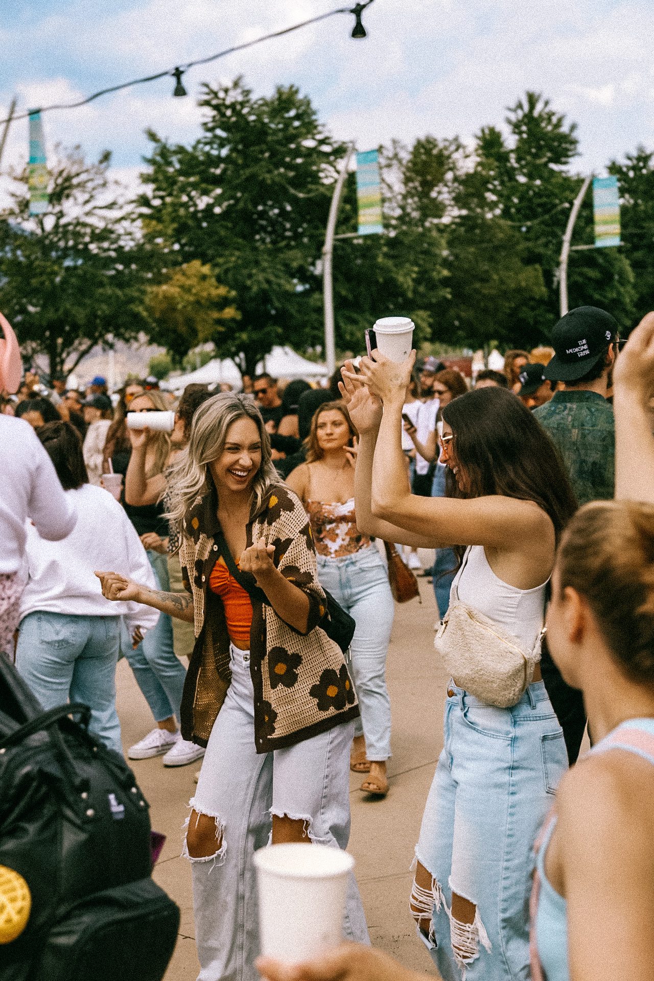 Two friends dancing with drinks on a sunny street